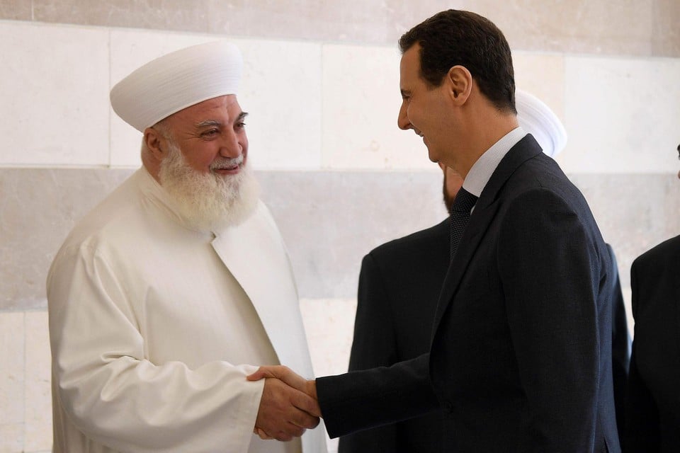 Op deze foto schudt Sjeikh Mohammed Adnan Afyoeni de hand van de Syrische president Bashar al-Assad. 