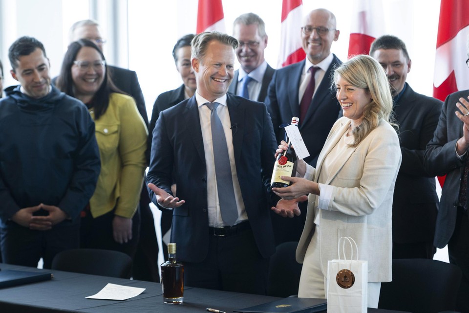 De Deense buitenlandminister Jeppe Kofod en Canadese buitenlandminister Melanie Joly wisselen flessen sterkedrank uit na de ondertekening van het akkoord. 
