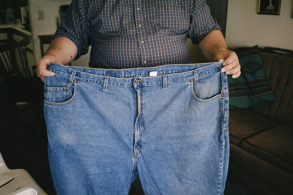 Een man toont aan de hand van zijn vroegere jeansbroek hoeveel hij is afgevallen.